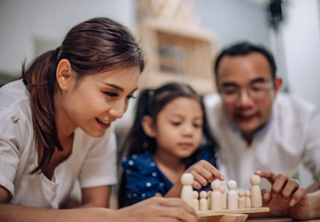 Parents and child playing with wooden family figures together at home, representing a nurturing environment when choosing the best childcare for early learning and development.