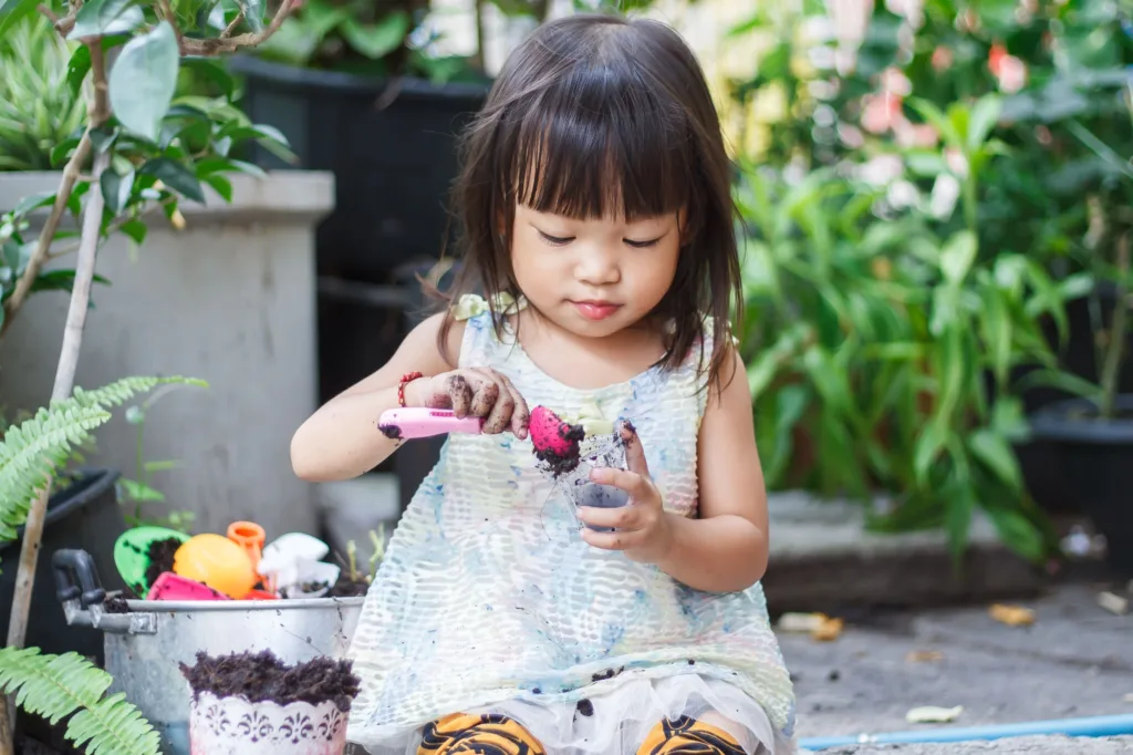 Young child engaged in outdoor play, planting and exploring soil with small gardening tools in a natural setting.