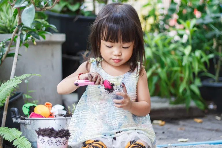 Young child engaged in outdoor play, planting and exploring soil with small gardening tools in a natural setting.